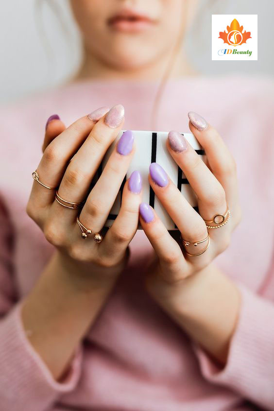 Bàn tay được làm nail màu nâu vàng, cầm một quả cam tươi trên nền vải họa tiết bắt mắt
