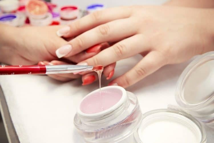 Bàn tay với móng tay giả đang bị tổn thương, cho thấy nguy cơ nhiễm trùng khi sử dụng móng nhân tạo không đúng cách