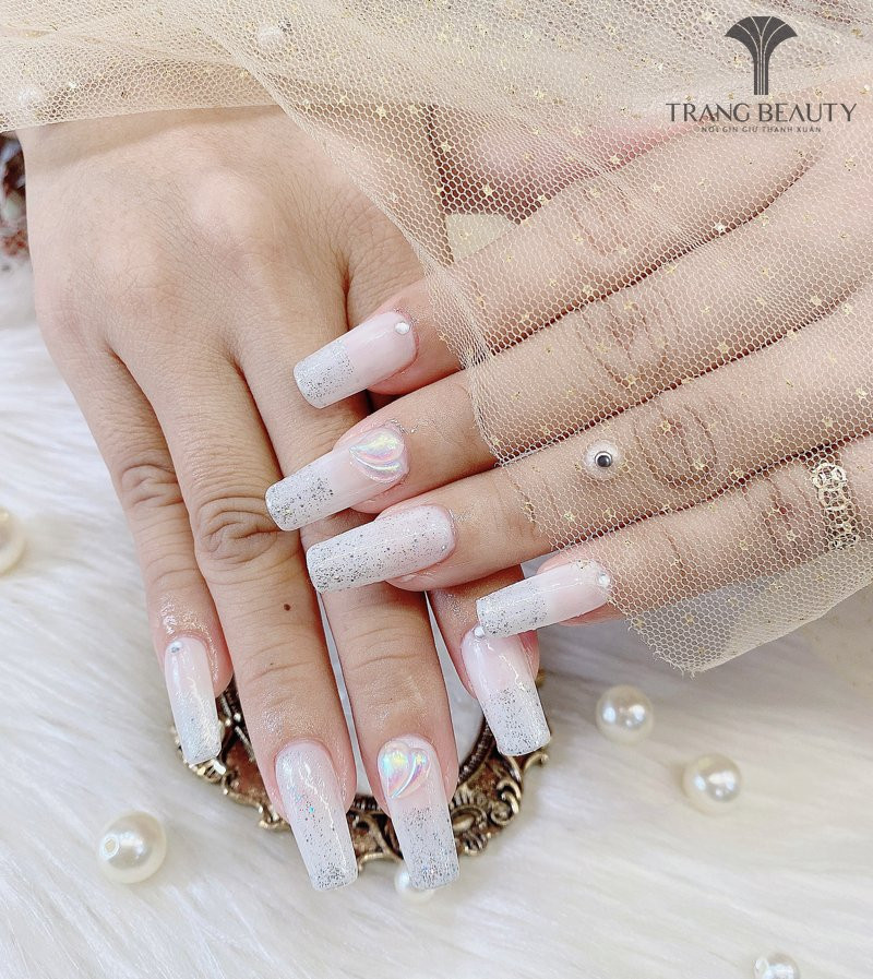 Bộ móng tay màu trắng gạo với kim tuyến màu bạc lấp lánh, tạo hiệu ứng long lanh và thu hút