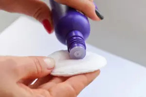 Đổ dung dịch tẩy móng chứa acetone lên miếng bông gòn để chuẩn bị làm sạch vết sơn trên quần áo