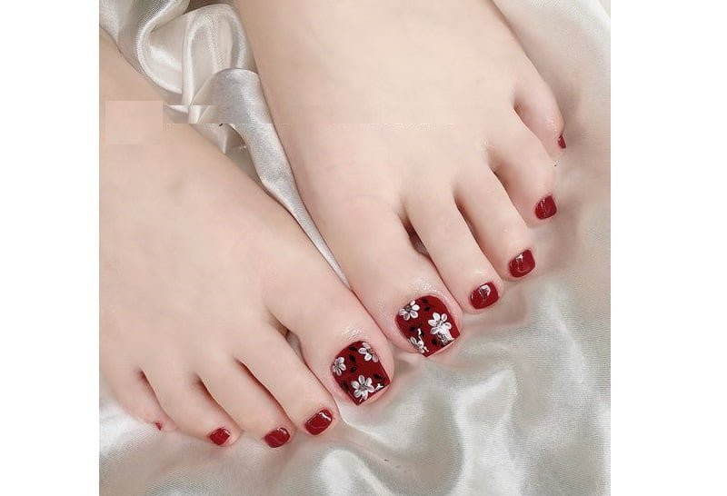Mẫu móng chân vẽ hoa trắng mềm mại trên nền đỏ sẫm, mang vẻ đẹp truyền thống nhưng nổi bật