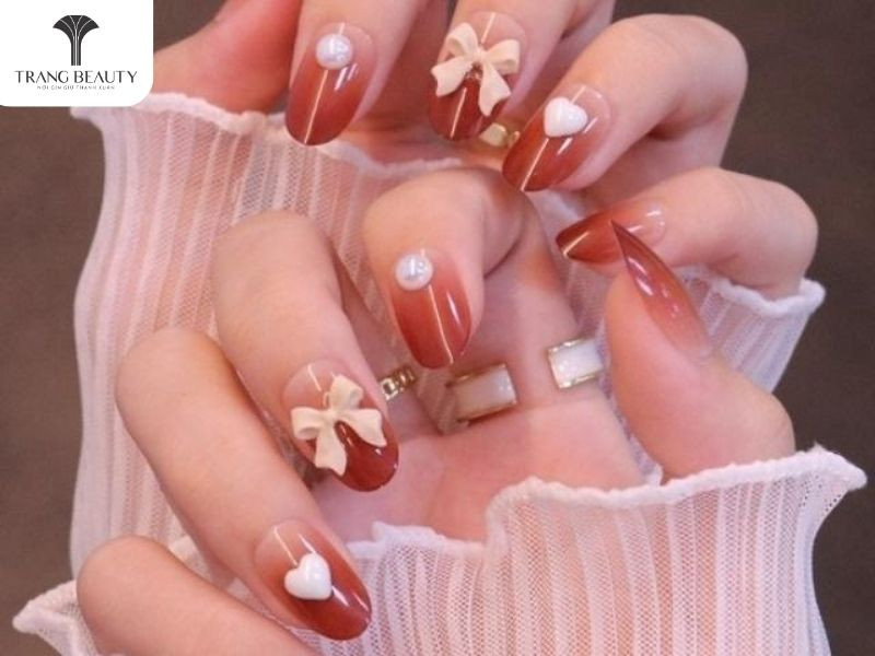 móng tay đính nơ hồng trên nền đỏ ombre với charm nơ và đá