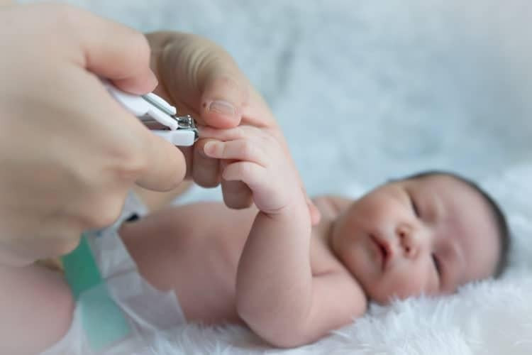 Một bà mẹ đang nhẹ nhàng thực hiện cách bấm móng tay cho bé sơ sinh một cách cẩn thận.