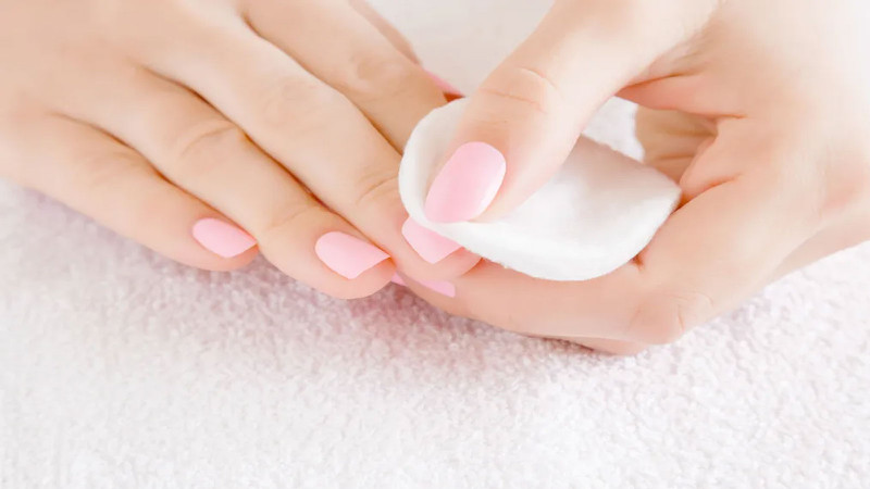 Người phụ nữ đang sử dụng bông thấm dung dịch tẩy sơn móng tay chuyên dụng để loại bỏ lớp sơn cũ khỏi móng tay một cách nhẹ nhàng.