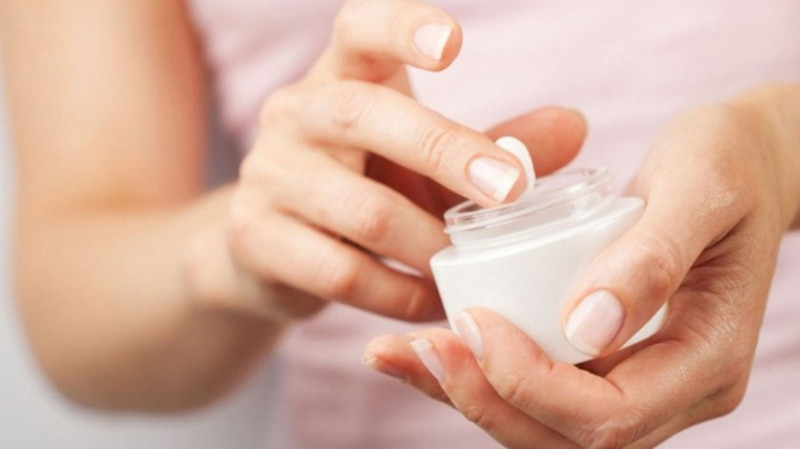 Người phụ nữ đang thoa kem dưỡng ẩm cho tay và móng, giúp khắc phục tình trạng móng tay mềm, dễ gãy do thiếu độ ẩm.