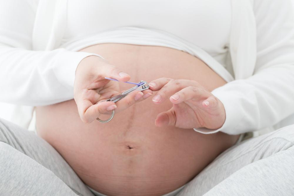 Người phụ nữ mang thai đang cắt móng tay cẩn thận, minh họa việc bà bầu có được cắt móng tay không một cách an toàn.