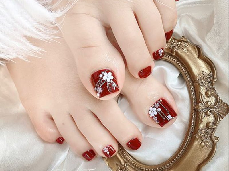 Thiết kế hoa móng chân đơn giản trên nền đỏ đô với họa tiết hoa trắng tinh tế